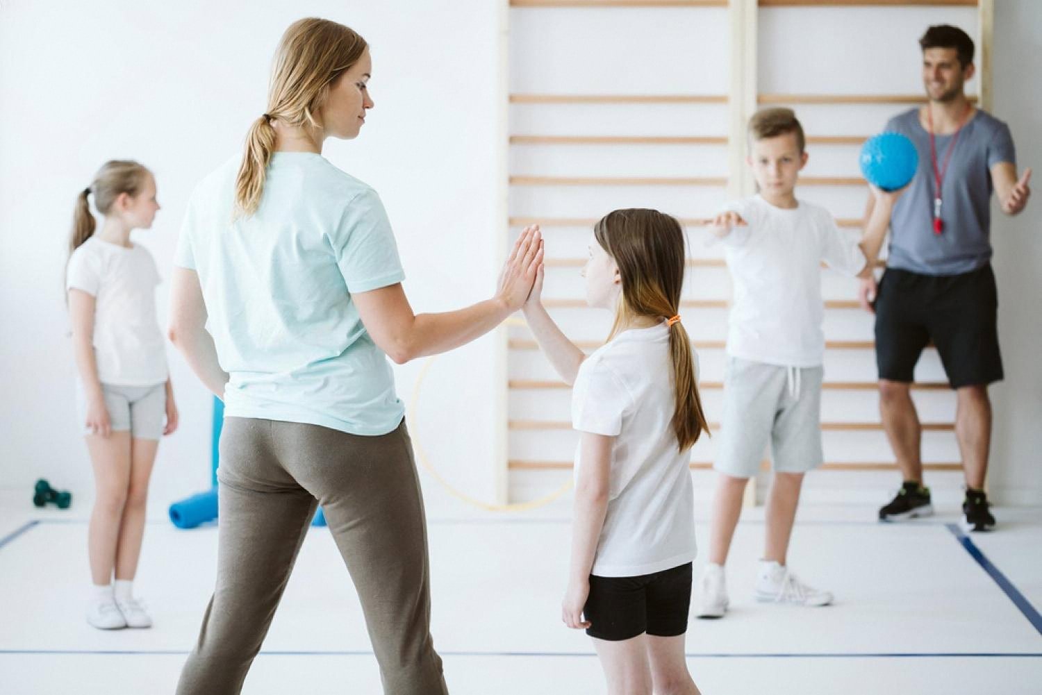 Coach high-fives a young girl during a school sports class with other children